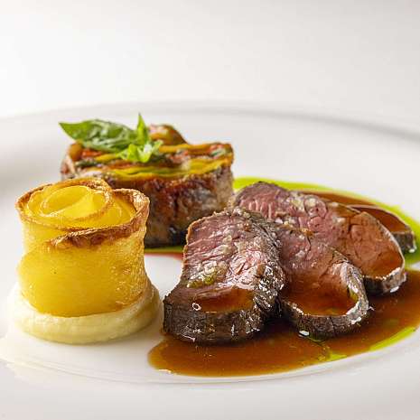 A chef pours sauce over an artfully arranged dish.