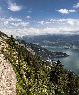 Blick auf einen Bergpfad mit Bänken und See im Hintergrund.