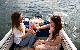 Zwei Frauen stoßen mit Gläsern auf einem Boot an.