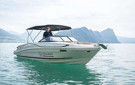 Ein Boot mit einem Steuermann auf klarem Wasser und Bergen im Hintergrund.