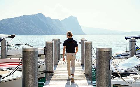 Ein Mann geht auf einem Steg zwischen Booten in Richtung Wasser.