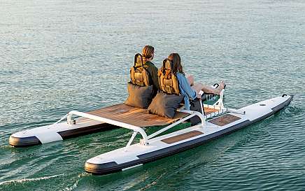 Zwei Personen sitzen auf einem modernen Boot auf ruhigem Wasser.
