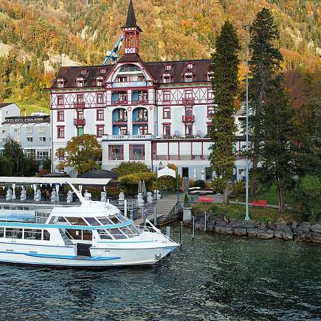 Abendaufnahme eines beleuchteten Stegs vor einem historischen Hotel mit Bergen im Hintergrund