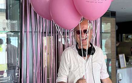 A DJ stands with pink balloons and a mixing console.