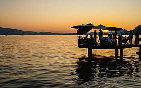 Menschen auf einem Steg genießen den Sonnenuntergang am See.