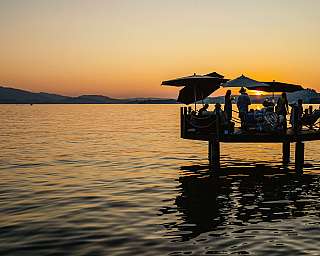 Menschen auf einem Steg genießen den Sonnenuntergang am See.