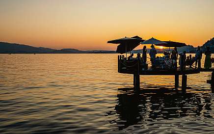 Menschen auf einem Steg genießen den Sonnenuntergang am See.