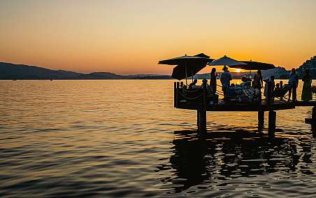 Menschen auf einem Steg genießen den Sonnenuntergang am See.