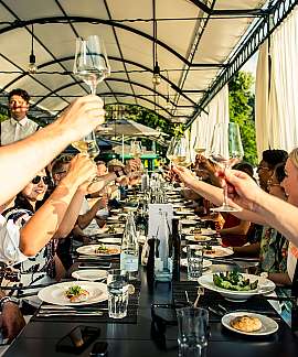 Gruppe von Menschen hebt Gläser bei einem festlichen Abendessen im Freien.