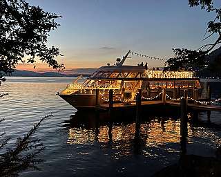 Boot mit Lichterketten am Steg bei Sonnenuntergang auf ruhigem Wasser
