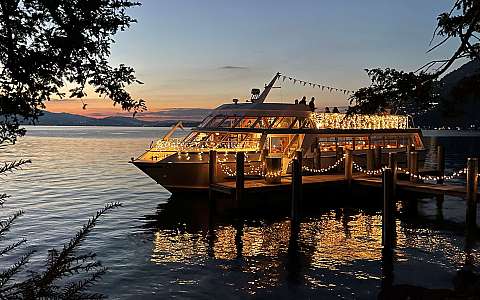 Boot mit Lichterketten am Steg bei Sonnenuntergang auf ruhigem See