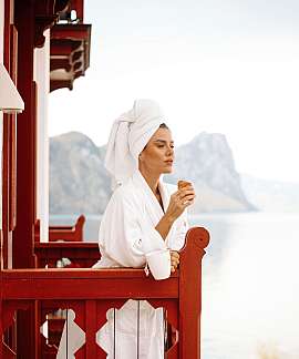 Frau in Bademantel genießt Croissant auf einem Balkon mit Bergblick.