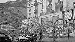 Gäste sitzen im Garten eines Hotels mit Bergblick.