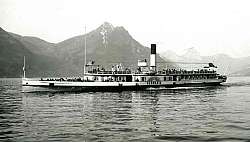 Dampfschiff Germania auf einem See mit Bergen im Hintergrund.