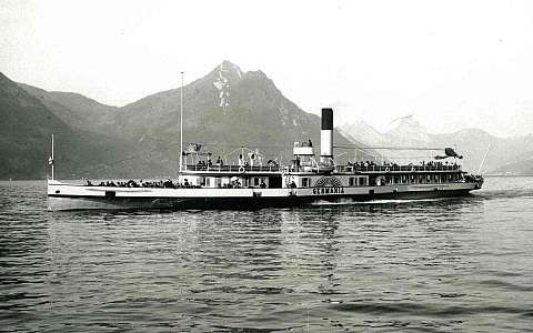 Ein Dampfschiff fährt auf einem ruhigen See mit Bergen im Hintergrund.