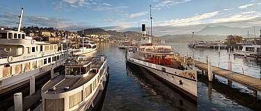 Blick auf den Hafen mit mehreren Booten und Bergen im Hintergrund.