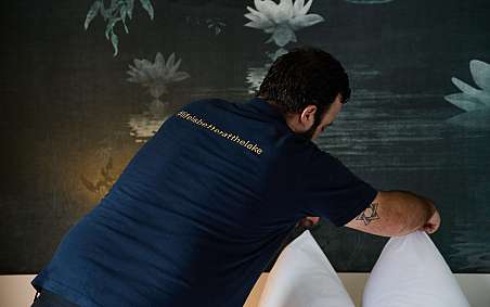 Ein Mitarbeiter richtet Kissen auf einem Bett in einem Hotelzimmer.