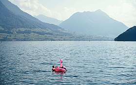 Eine Person schwimmt auf einem pinken Flamingo im Wasser.