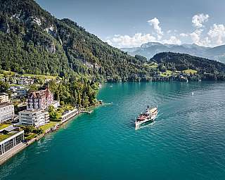 Ein Dampfschiff fährt auf einem klaren See, umgeben von Bergen.