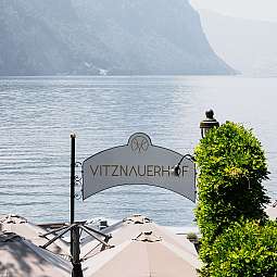 Blick auf den Vitznauerhof mit Bergen im Hintergrund und Sonnenschirmen.