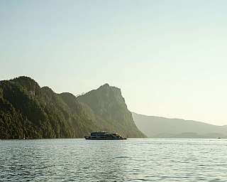 Ein Boot fährt auf einem ruhigen Gewässer mit Bergen im Hintergrund.