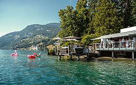 Menschen entspannen am See mit Schwimmreifen und Sonnenschirmen.