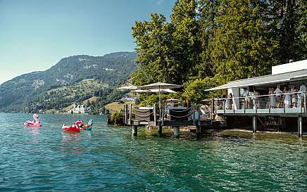 Menschen entspannen am See mit Schwimmreifen und Sonnenschirmen.
