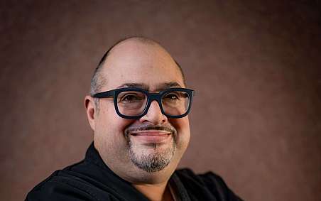 Two chefs are working intently with fresh herbs in a bowl.