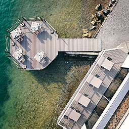 Luftaufnahme eines Holzstegs mit Tischen über klarem Wasser.
