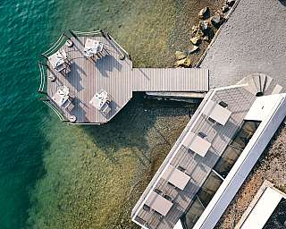 Luftaufnahme eines Holzstegs mit Tischen am Wasser.