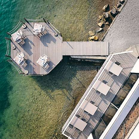 Aerial view of a wooden walkway with tables over clear water.