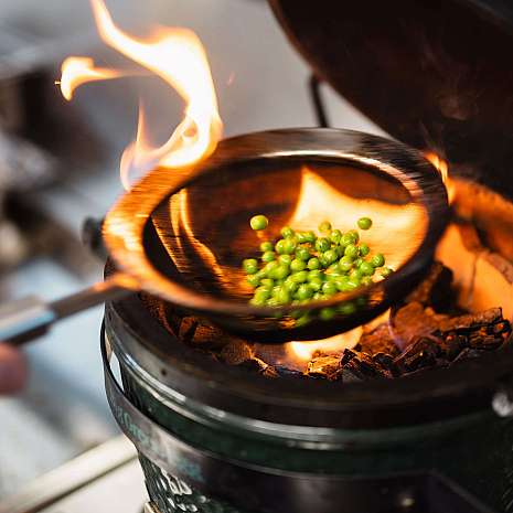 Grüne Erbsen werden über einer offenen Flamme in einer Pfanne zubereitet.