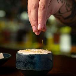 Eine Hand streut Gewürze auf einen Cocktail in einer Tasse.