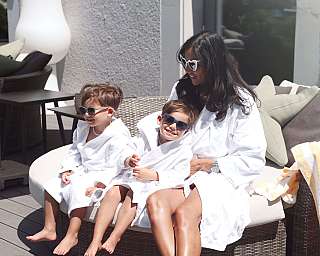 Eine Frau und zwei Kinder in Bademänteln und Sonnenbrillen auf einer Liege.