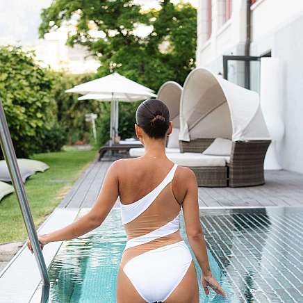 Eine Frau in einem weißen Badeanzug geht am Pool entlang.