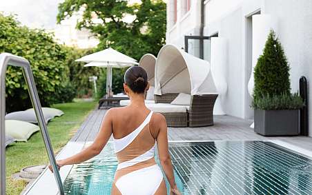 A woman in a white swimsuit walks along the pool.
