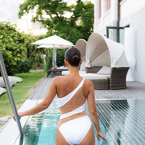 A woman in a white swimsuit walks along the pool.