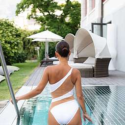 Eine Frau in einem weißen Badeanzug geht am Pool entlang.