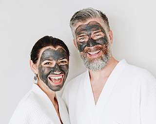 Lächelndes Paar mit schwarzen Gesichtsmasken in Bademänteln.