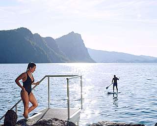 Eine Frau steht an einem Steg, während ein Paddler im Wasser ist.