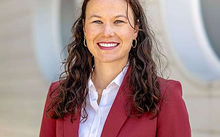 Porträt einer Frau in einem roten Blazer vor einer modernen Wand.