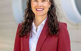 Porträt einer Frau in einem roten Blazer vor einer modernen Wand.