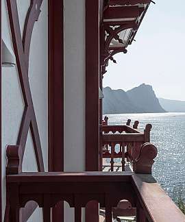 Blick von einem Balkon auf einen glitzernden See und Berge.
