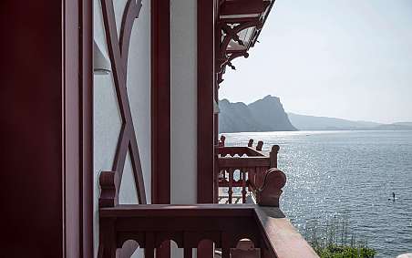 Blick von einem Balkon auf einen glitzernden See und Berge.