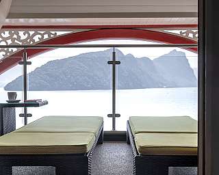 Zwei Liegen auf einem Balkon mit Blick auf das Meer und Berge.